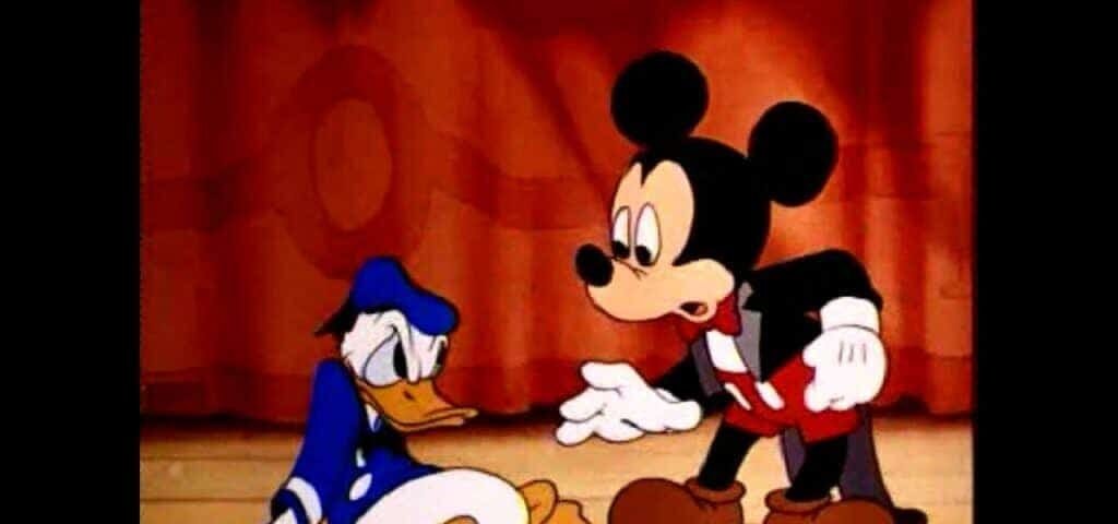 Mickey Mouse, dans son short rouge classique et ses gants blancs, semble consoler Donald Duck, qui a l'air bouleversé et est assis par terre devant un fond marron uni.