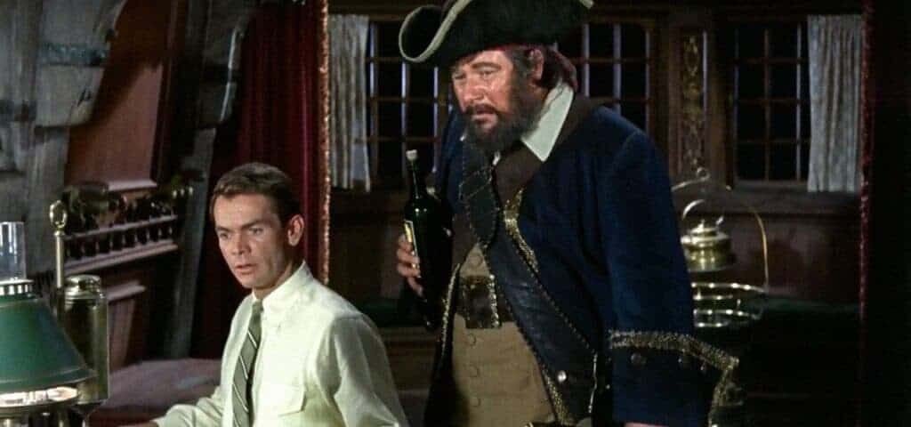 Une scène du classique de Disney "Le Fantôme de Barbe Noire" mettant en scène deux hommes : l'un vêtu d'une chemise claire et d'un pantalon foncé regarde avec appréhension l'autre, un homme robuste en