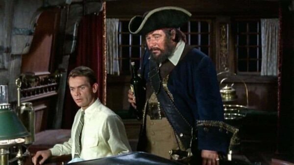 Une scène du classique de Disney "Le Fantôme de Barbe Noire" mettant en scène deux hommes : l'un vêtu d'une chemise claire et d'un pantalon foncé regarde avec appréhension l'autre, un homme robuste en