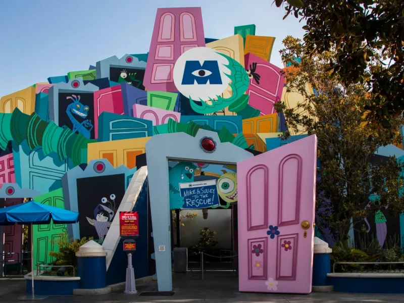 Une façade colorée et caricaturale représentant des éléments de construction surdimensionnés comme des fenêtres et des portes, conçue de manière créative comme l'entrée de l'attraction Monsters Inc : Mike & Sulley to the Rescue!".