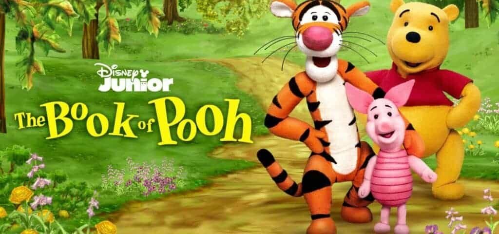 Image promotionnelle du "livre de Winnie l'ourson" montrant Tigrou, l'ourson et Porcinet debout ensemble dans un décor de forêt verdoyante et vibrante, avec le logo Disney Junior