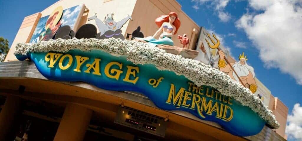 L'entrée de l'attraction "Voyage de la Petite Sirène" dans un parc à thème Disney, avec une sculpture colorée d'Ariel et des personnages marins au-dessus du panneau.