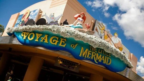 L'entrée de l'attraction "Voyage de la Petite Sirène" dans un parc à thème Disney, avec une sculpture colorée d'Ariel et des personnages marins au-dessus du panneau.