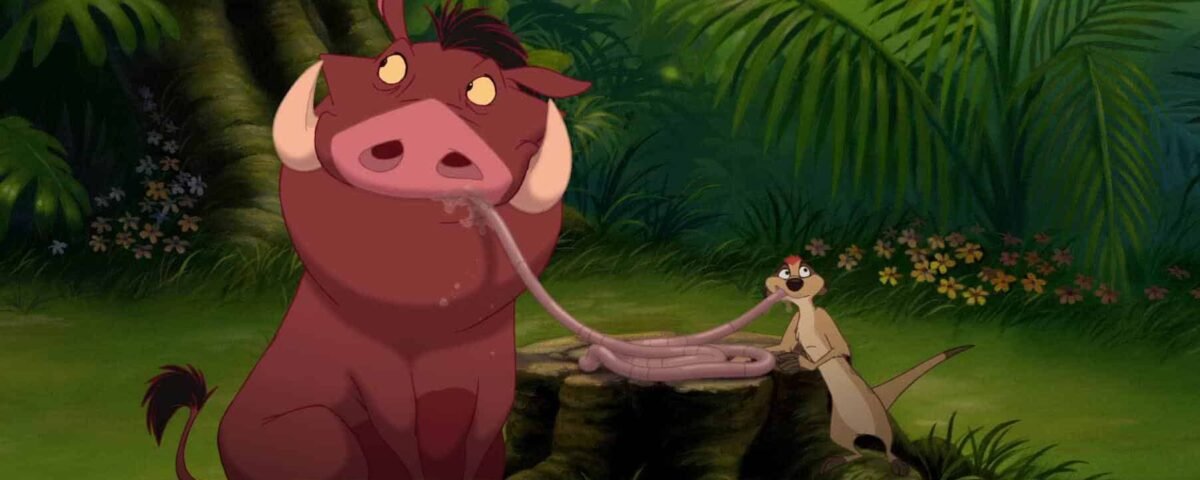 Image animée de "Le Roi Lion 3" représentant un grand phacochère brun et un mince suricate beige dans une jungle luxuriante. Le phacochère semble confus alors que