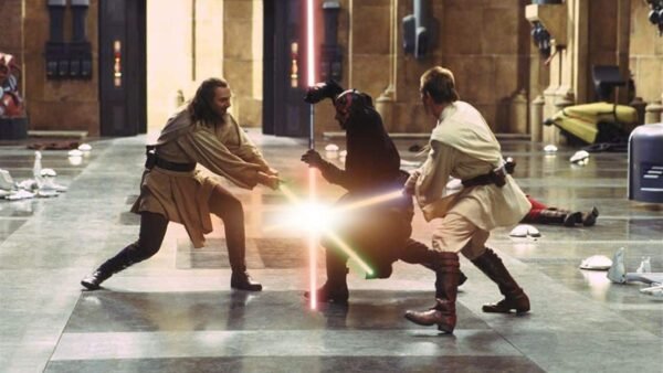 Deux Jedi, l'un avec un sabre laser bleu et l'autre avec un sabre laser vert, affrontent un Seigneur Sith brandissant un sabre laser rouge à double lame dans un grand couloir de "La Menace Fantôme".