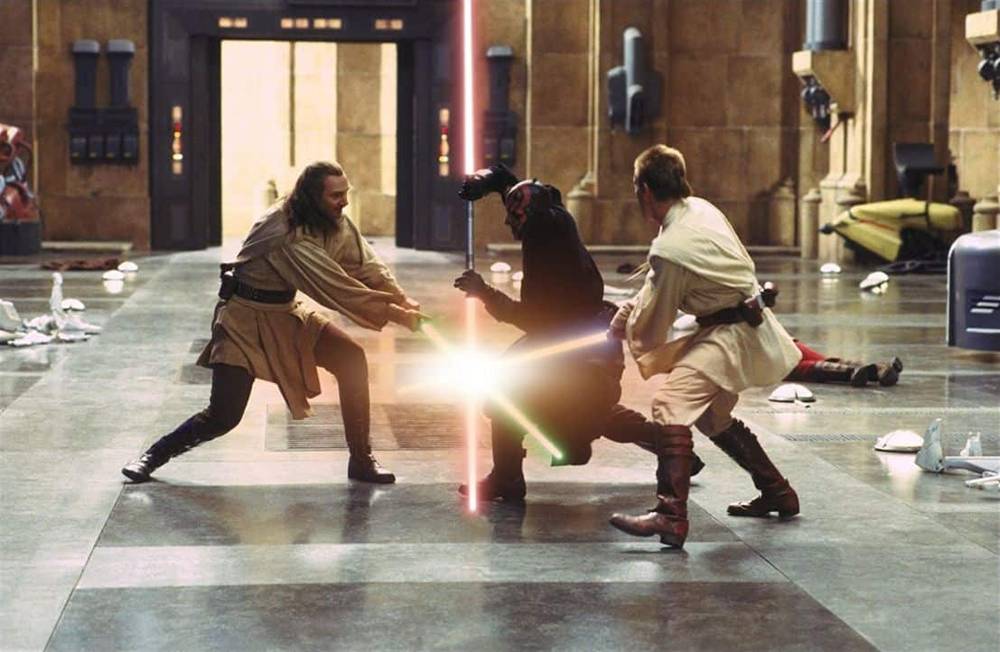 Deux Jedi, l'un avec un sabre laser bleu et l'autre avec un sabre laser vert, affrontent un Seigneur Sith brandissant un sabre laser rouge à double lame dans un grand couloir de "La Menace Fantôme".
