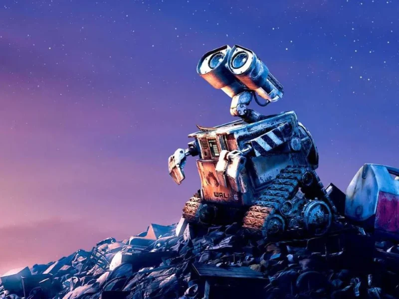 Une photo du robot animé Wall E assis sur un gros tas d'ordures sous un ciel étoilé au crépuscule, l'air pensif et curieux.