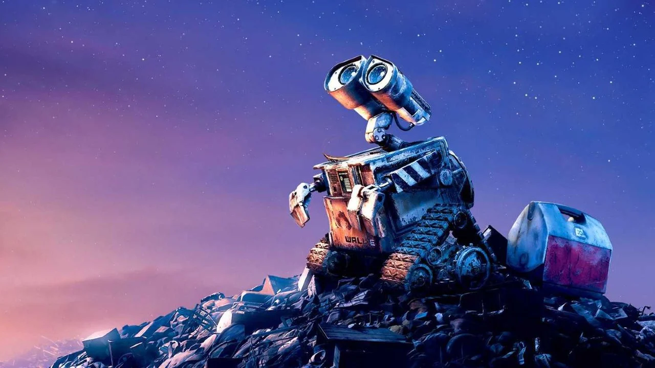 Une photo du robot animé Wall E assis sur un gros tas d'ordures sous un ciel étoilé au crépuscule, l'air pensif et curieux.