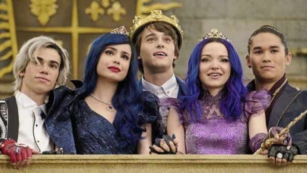 Cinq jeunes acteurs se faisant passer pour des descendants de membres de la famille royale dans une scène de film fantastique, portant des costumes et des couronnes ornés, dans une somptueuse salle dorée, exprimant une joyeuse camaraderie.