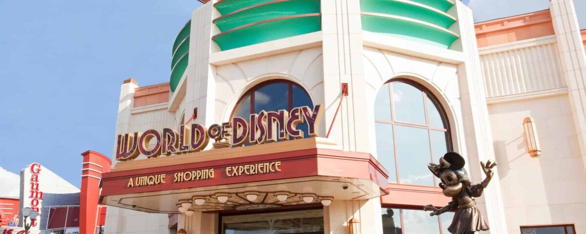Vue extérieure du magasin "World of Disney" avec une statue de Mickey Mouse accueillant les visiteurs, une architecture colorée, sous un ciel dégagé.