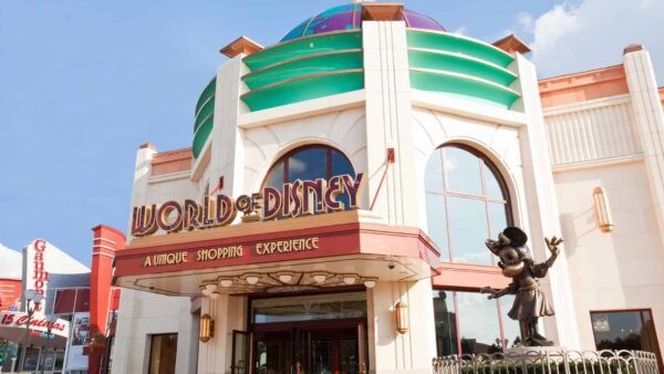 Vue extérieure du magasin "World of Disney" avec une statue de Mickey Mouse accueillant les visiteurs, une architecture colorée, sous un ciel dégagé.