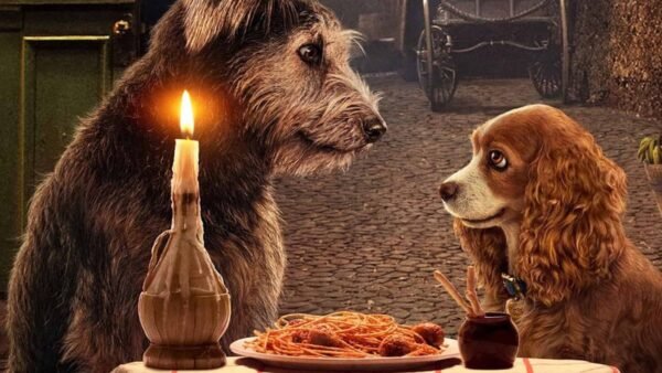 Deux chiens, un grand débraillé et un plus petit bronzé, assis à une table avec une assiette de spaghetti et une bougie allumée, partageant un dîner romantique rappelant "La Belle et