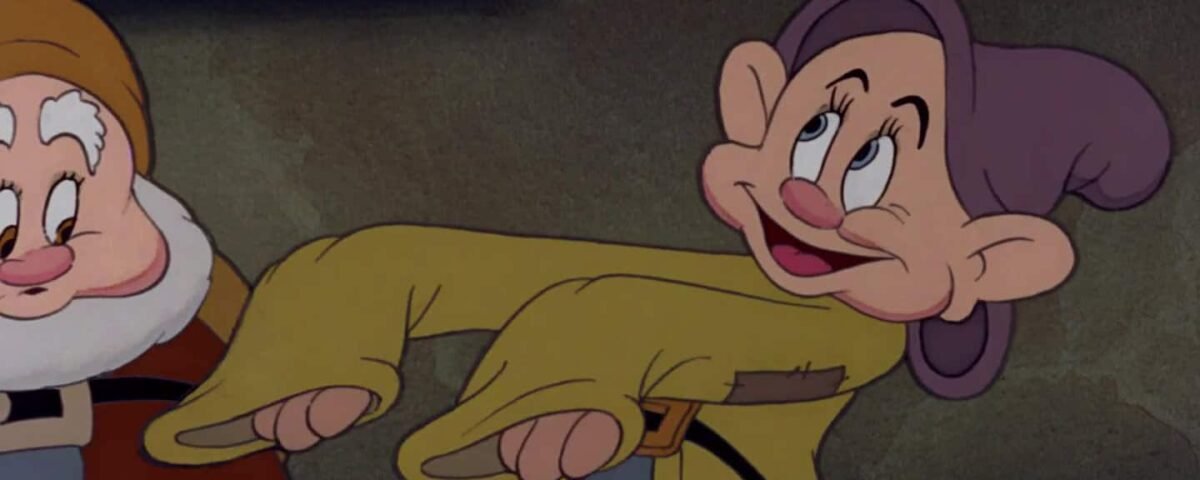 Deux nains animés d'un film classique, dont l'un regarde jovialement Simplet, qui coud un patch sur son propre pantalon déchiré.