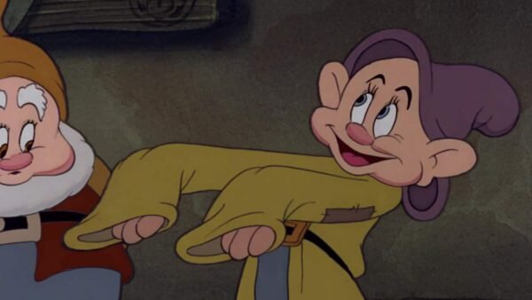 Deux nains animés d'un film classique, dont l'un regarde jovialement Simplet, qui coud un patch sur son propre pantalon déchiré.