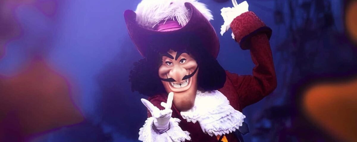 Une personne habillée en Capitaine Crochet, posant avec un geste de la main et un sourire narquois, portant un grand chapeau rouge, un manteau rouge foncé à volants blancs et tenant un crochet dans l'autre