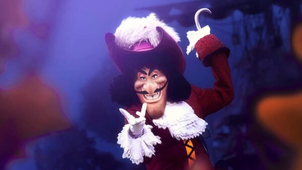 Une personne habillée en Capitaine Crochet, posant avec un geste de la main et un sourire narquois, portant un grand chapeau rouge, un manteau rouge foncé à volants blancs et tenant un crochet dans l'autre