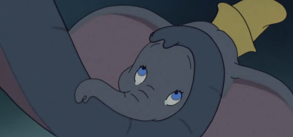 Une image de dessin animé de Dumbo, le petit éléphant des chansons de Disney, l'air triste et reposant sa tête et sa trompe sur ses jambes croisées, avec un petit chapeau jaune sur la tête.
