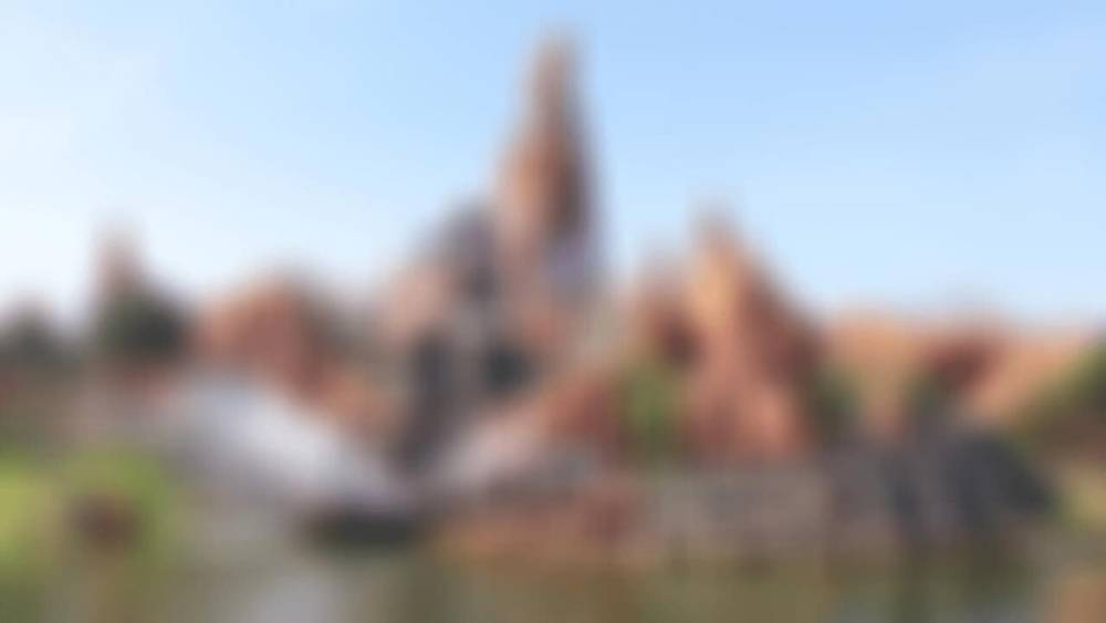 Image floue d'une scène extérieure pittoresque à Disneyland Paris, comportant éventuellement de l'eau, des structures et de la verdure, rendant des détails spécifiques indistincts.