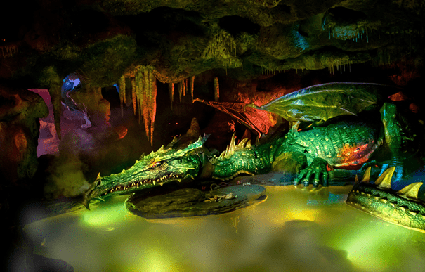 Un dragon vert dans une grotte sombre avec des personnages mystérieux.