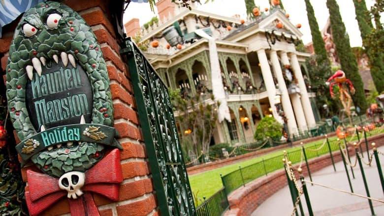 Un panneau d'entrée décoré pour le "Phantom Manor" avec des yeux et des dents effrayants, sur fond de manoir orné de décorations festives mais étranges d'Halloween à Disneyland Paris.