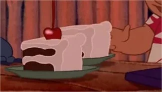 Une tranche de gâteau animé avec un glaçage blanc et une cerise sur le dessus est posée sur une assiette, à côté de la main d'un personnage tendu vers elle, avec un rideau en toile de fond dans une scène de Plats Films Disney