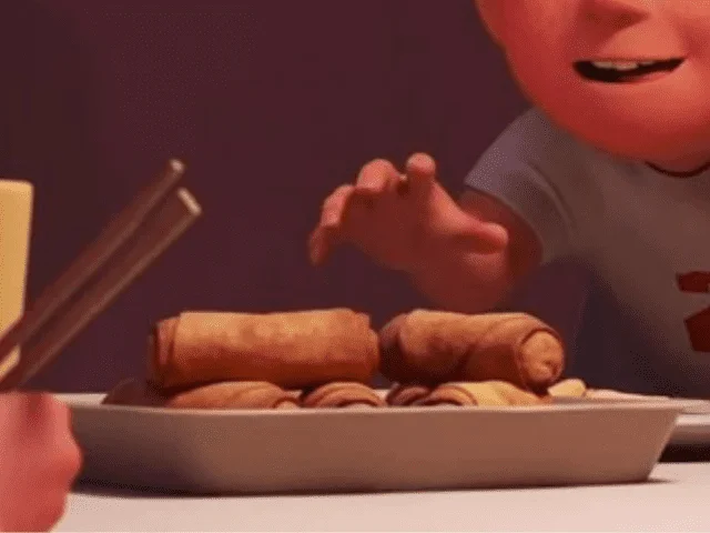 Une scène animée présentant une vue rapprochée d'une assiette de pâtisseries roulées avec la main d'un personnage de Disney tendue vers eux, indiquant l'empressement ou le plaisir de les manger.