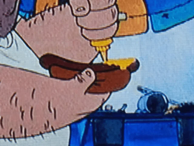 Image de dessin animé représentant une main utilisant un tournevis sur un objet en bois, avec un fond bleu encombré suggérant un décor d'atelier Disney.