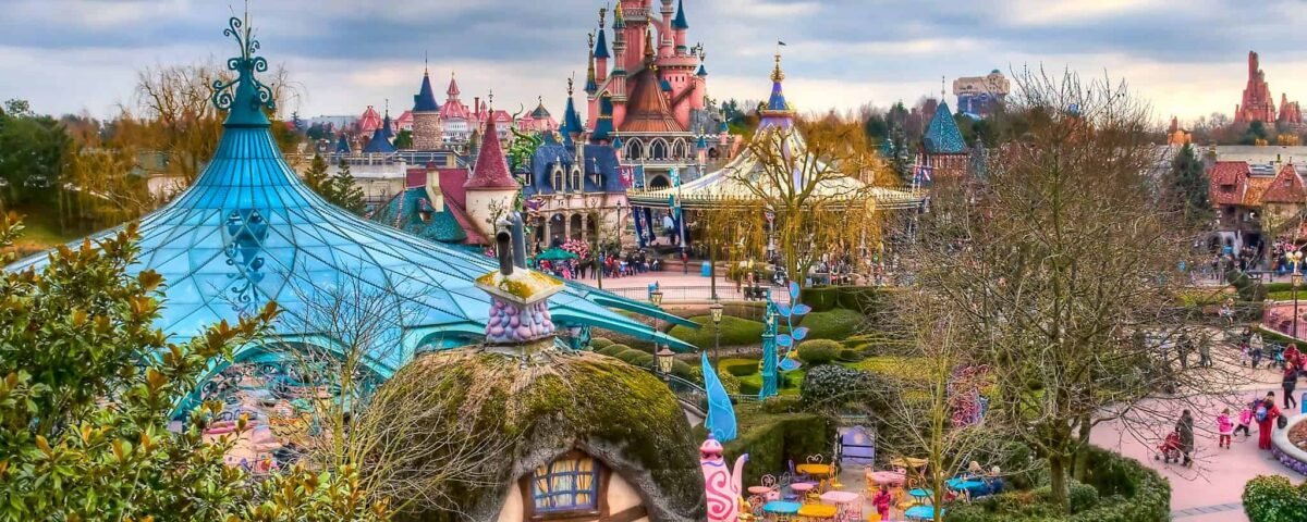 Une image vibrante de Disneyland Paris, mettant en valeur l'emblématique château rose de la Belle au bois dormant avec des détails exquis en arrière-plan et un parc animé rempli de visiteurs et de décorations colorées.