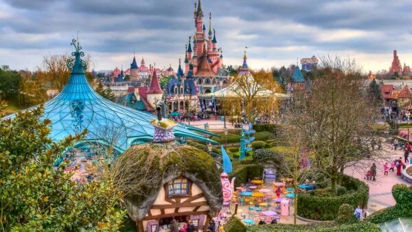 Une image vibrante de Disneyland Paris, mettant en valeur l'emblématique château rose de la Belle au bois dormant avec des détails exquis en arrière-plan et un parc animé rempli de visiteurs et de décorations colorées.