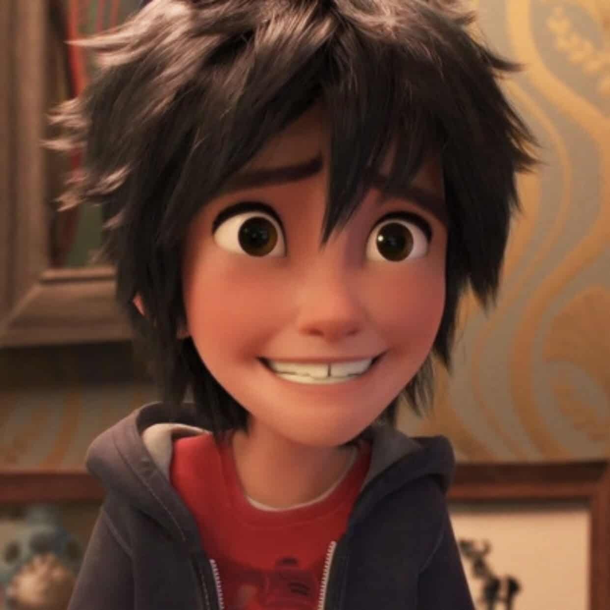 Gros plan d'un jeune personnage animé de Disney aux cheveux noirs hérissés et aux grands yeux verts, souriant largement. Il porte un t-shirt rouge sous un sweat à capuche bleu.