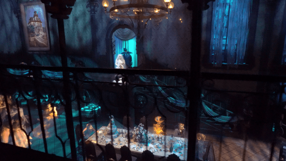 Une pièce atmosphérique et faiblement éclairée au sein du Phantom Manor, décorée avec des meubles vintage et des personnages fantomatiques et éthérés autour d'une somptueuse table à manger, générant une ambiance hantée et étrange.