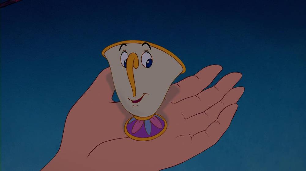 Une main humaine tenant doucement Chip, le petit personnage mignon et animé d'une tasse de thé avec un visage et une puce sur le bord, de « La Belle et la Bête » de Disney.
