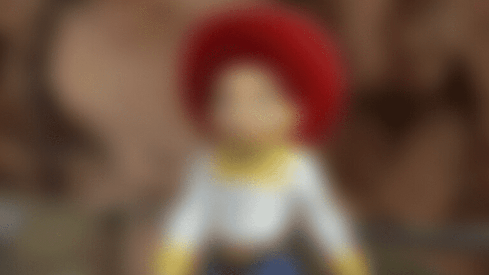Image floue d'une figurine ressemblant à un personnage de Disneyland Paris vêtue de vêtements colorés de style médiéval, avec un chapeau rouge proéminent. L’arrière-plan est légèrement flou.