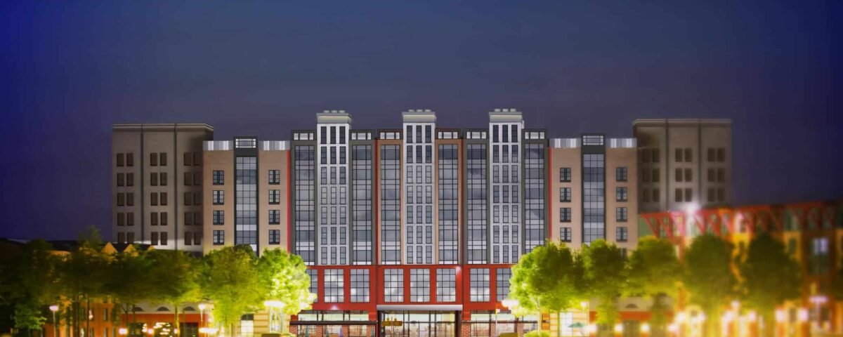 Vue nocturne d'un immeuble d'appartements moderne avec des fenêtres éclairées, comportant une section centrale rouge, flanquée d'ailes plus hautes et symétriques, se reflétant dans un plan d'eau calme au premier plan.