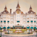 L'image montre le majestueux Disneyland Hotel de Disneyland Paris au coucher du soleil avec un ciel dégagé. L'hôtel présente une architecture élégante d'inspiration victorienne avec plusieurs tourelles et balcons.