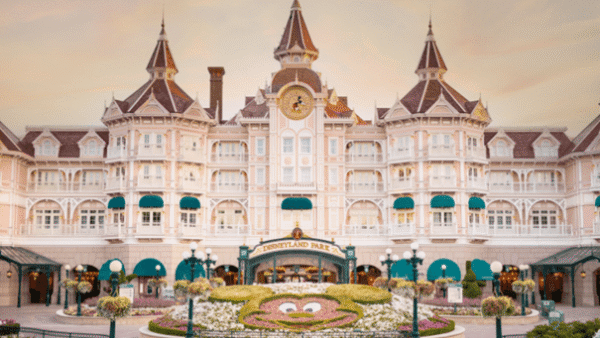 L'image montre le majestueux Disneyland Hotel de Disneyland Paris au coucher du soleil avec un ciel dégagé. L'hôtel présente une architecture élégante d'inspiration victorienne avec plusieurs tourelles et balcons.