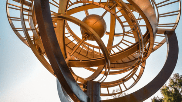 Grande sculpture cinétique comportant des anneaux métalliques circulaires et un orbe central doré, sur un ciel bleu. Le mot « Discoveryland » est affiché bien en évidence en bas.