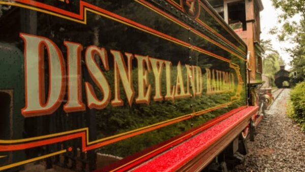 Gros plan du train ferroviaire de Disneyland Paris avec des détails vibrants et une finition brillante, garé sur des voies entourées d'une verdure luxuriante.