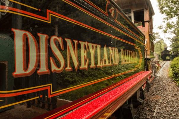 Gros plan du train ferroviaire de Disneyland Paris avec des détails vibrants et une finition brillante, garé sur des voies entourées d'une verdure luxuriante.
