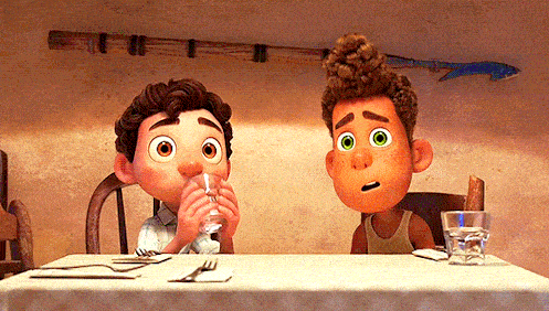 Deux garçons animés autour d'une table, l'un buvant de l'eau pendant qu'un poisson passe, les laissant tous deux surpris dans l'ambiance chaleureuse et cosy du décor du film "Luca".