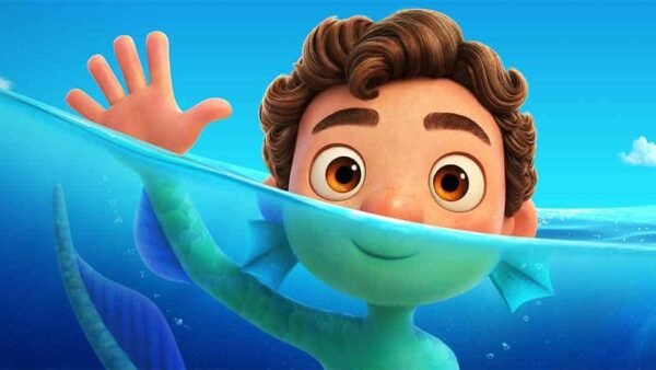 Scène animée du film *Luca* mettant en vedette un jeune garçon aux cheveux bouclés partiellement immergé dans l'eau, souriant et saluant, tandis qu'une sympathique créature marine enroule un tentacule autour de sa main contre un fond lumineux.