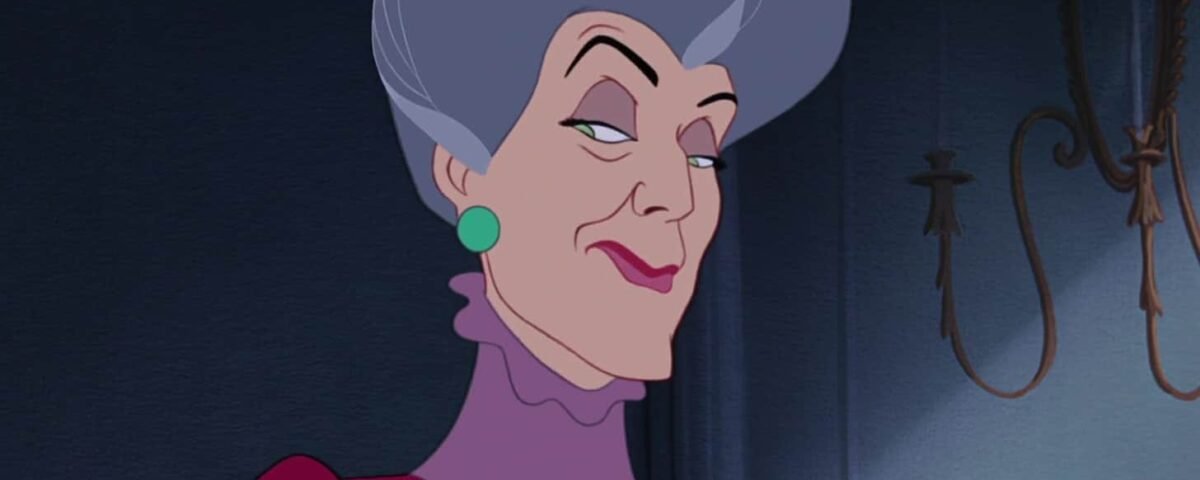 Illustration de Lady Tremaine, une des Méchants Disney, souriante ; elle a les cheveux gris, porte une robe marron et des boucles d'oreilles vertes sur un fond sombre.
