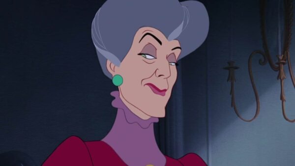Illustration de Lady Tremaine, une des Méchants Disney, souriante ; elle a les cheveux gris, porte une robe marron et des boucles d'oreilles vertes sur un fond sombre.
