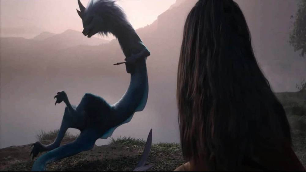 Une jeune femme aux cheveux longs regarde un dragon bleu étirant son cou et ses ailes au bord d'un lac brumeux à l'aube dans "Raya et le Dernier Dragon.