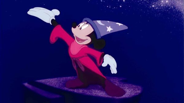 Souris, habillée en apprenti sorcier avec une robe rouge et un chapeau bleu avec des étoiles blanches, se tient sur une plate-forme de pierre sous un ciel étoilé, agitant dramatiquement la main.