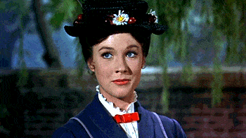 Mary Poppins, vêtue d'un manteau et d'un chapeau bleus, regarde directement la caméra avec un léger sourire et apparaît comme si elle était sur le point d'entamer des chansons de Disney, entourée d'un fond de jardin légèrement flou.