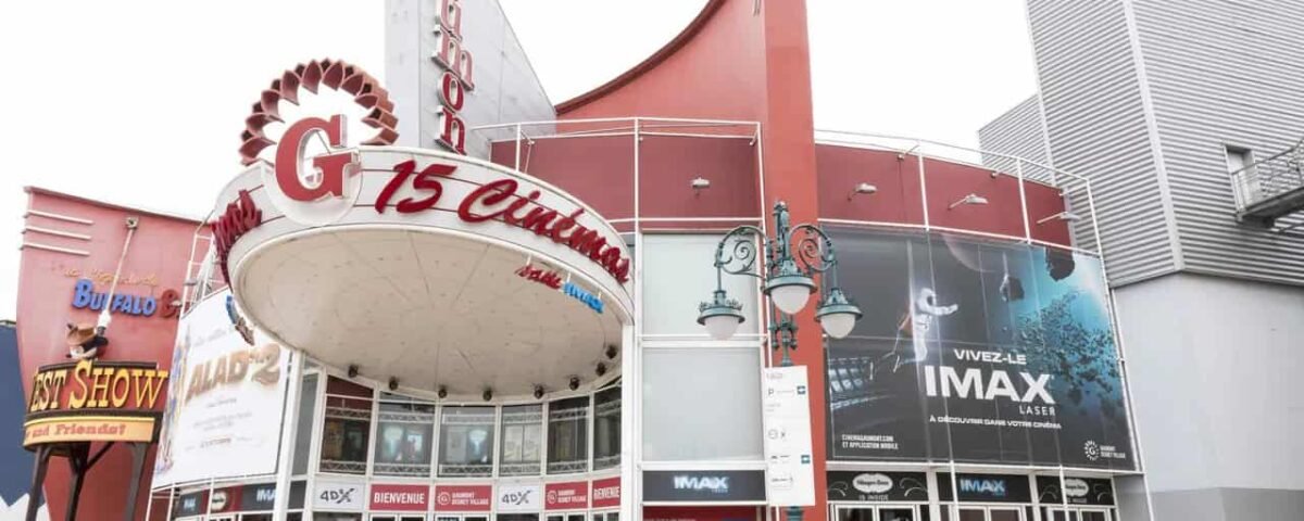 Extérieur du cinéma Gaumont avec un grand chapiteau de style rétro avec des néons, plusieurs affiches et un ciel bleu clair au-dessus.
