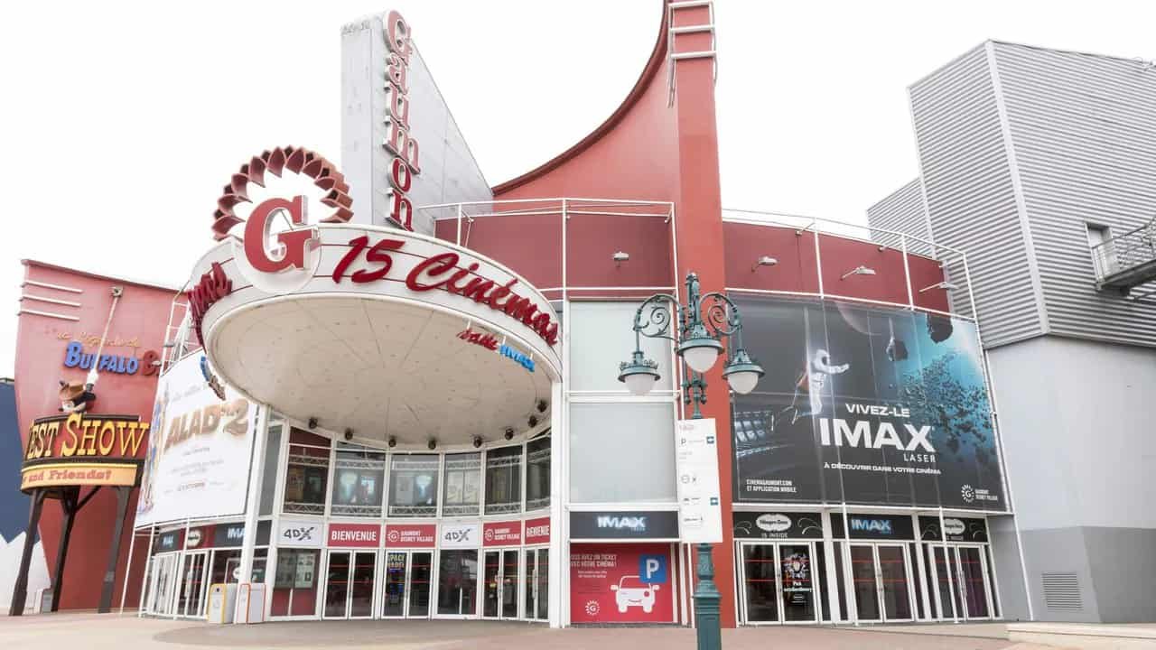 Extérieur du cinéma Gaumont avec un grand chapiteau de style rétro avec des néons, plusieurs affiches et un ciel bleu clair au-dessus.
