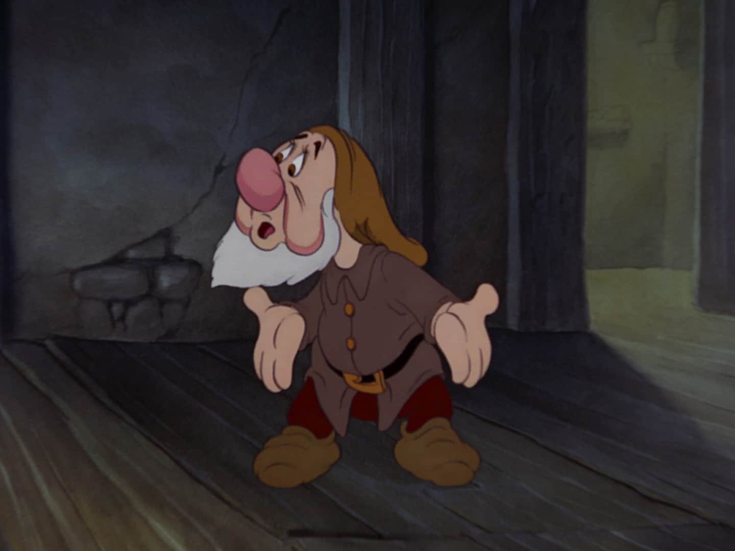 Une image animée de Grumpy, un nain de « Blanche-Neige » de Disney, debout dans une pièce faiblement éclairée, l'air mécontent, les bras croisés et le visage froncé.