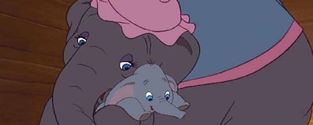 Une image tirée du film d'animation "Dumbo" montrant un bébé éléphant bercé de manière protectrice sous la trompe d'un éléphant plus grand, tous deux portant des accessoires de cirque roses.